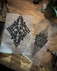 two pieces of paper with designs on them sitting on a table next to some scissors