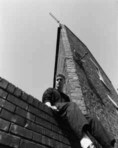 a man sitting on top of a brick wall next to a tall building with an antenna