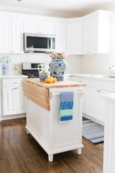 a kitchen with white cabinets and wood flooring is pictured in this image, there are blue and white vases on the island