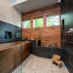 a modern bathroom with wood paneling and black tile on the walls, along with a large bathtub