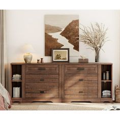 a wooden dresser sitting next to a bed in a room with white walls and paintings on the wall