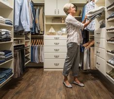 a woman standing in front of a closet filled with clothes and folded up shirts on hangers