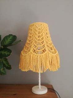 a crocheted lamp shade sitting on top of a wooden table next to a potted plant