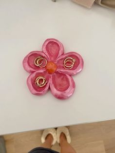 a pink flower brooch sitting on top of a white table next to a pair of shoes