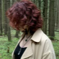 a woman with red hair standing in the woods