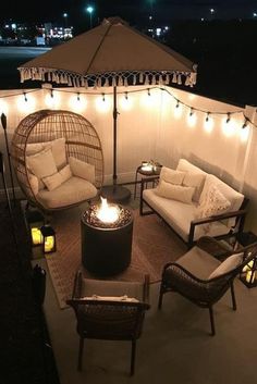 an outdoor seating area is lit up at night with string lights on the ceiling and chairs around it