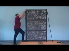 a man standing on top of a wooden floor next to a tall metal paneled screen