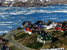 many houses on the side of a road near water and mountains with icebergs in the background