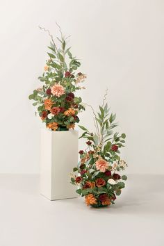 two white vases filled with flowers and greenery