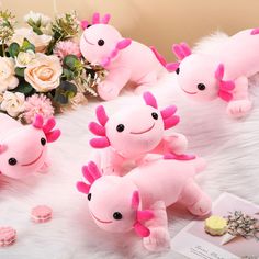 several pink stuffed animals sitting on top of a white fur covered floor next to flowers