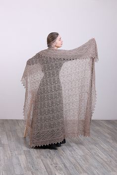 a woman standing in front of a white wall wearing a shawl