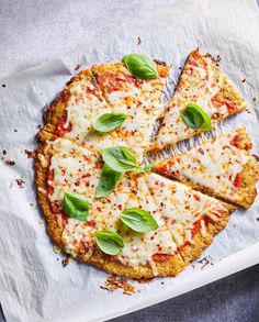 a pizza with cheese and basil on top is cut into four slices, sitting on a piece of parchment paper