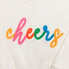 a white sweatshirt with the word cheers painted on it's chest and colorful letters across the chest