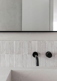 a bathroom sink with two black faucets and a mirror above it, in front of a white tiled wall