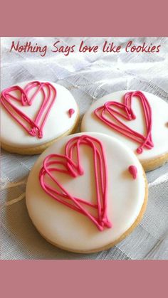 three decorated cookies with pink icing sitting on a table cloth next to each other