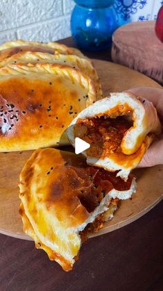 a person holding a piece of food on top of a wooden plate next to another pie