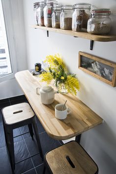 there is a table with some jars on it next to two stools and a window