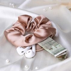 a pink scrunffle on top of a white satin material with headphones and money