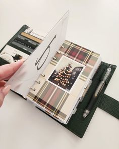 a hand holding an open book with pictures on it and a pen next to it