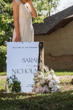 a woman standing in front of a sign talking on a cell phone while wearing a white dress