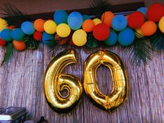 balloons and streamers decorate the backdrop for a 60th birthday party with gold foil numbers