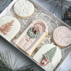 four decorated cookies in a box with pine cones on the top one is pink and white