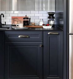 a kitchen with black cabinets and white tile backsplashing, stainless steel appliances