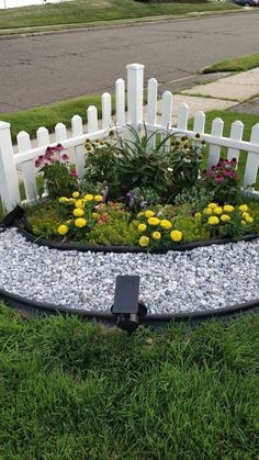 a white picket fence and flower bed in the grass