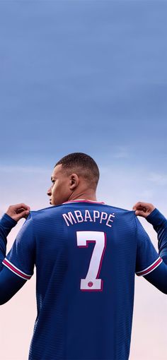 a man holding onto his jersey while standing in front of a blue and white sky