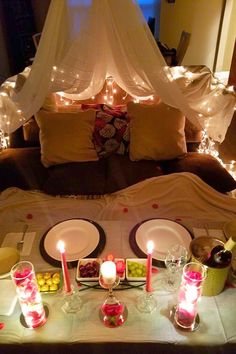 the table is set with candles, plates and fruit in front of a canopy bed