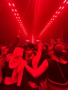 a group of people standing in a room with red lights on the ceiling and their hands up