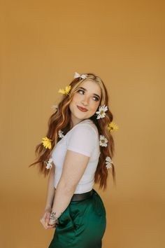 a woman with flowers in her hair poses for a photo wearing a white shirt and green skirt