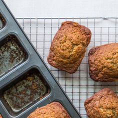 freshly baked muffins cooling on a wire rack next to a baking pan with more muffins in it