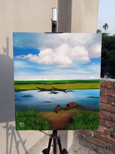 a painting is being displayed on a tripod in front of a brick wall and water