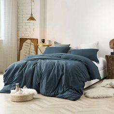 a bed with blue sheets and pillows in a white room next to a wooden table