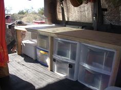 the inside of a van with plastic containers and drawers on the back door, while two people sit in the background