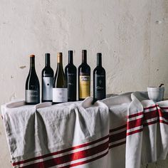 five bottles of wine are lined up on a tablecloth with a cup and saucer