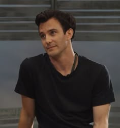 a man in black shirt sitting down with his hand on his hip and looking at the camera