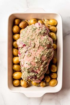 meat and potatoes in a casserole dish on a marble countertop, with herbs sprinkled over the top