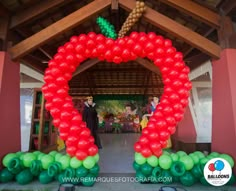 an arch made out of balloons in the shape of a large red apple with green leaves