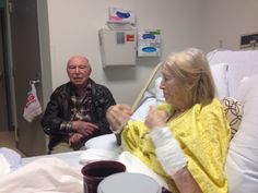 a man and woman sitting in a hospital bed with one holding a glass of wine