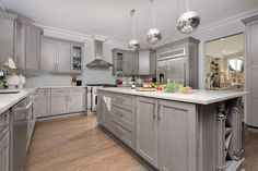 a large kitchen with stainless steel appliances and wooden floors, along with white counter tops