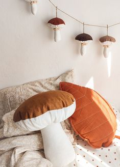 pillows on a bed with mushrooms hanging from the wall behind them and in front of it is a string of lights