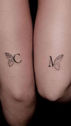 two tattoos on the legs of women with butterfly wings and letter m in black ink