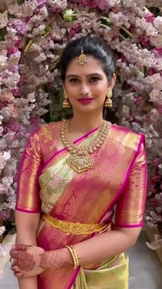 a woman in a yellow and pink sari with gold jewelry on her neck, standing next