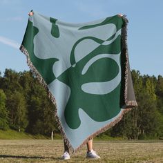 a person holding up a green and white blanket in front of some trees on a sunny day