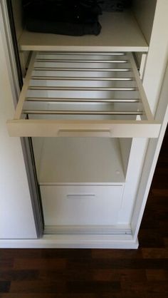 an open refrigerator door in a kitchen with wood flooring and white walls, showing the bottom shelf filled with items