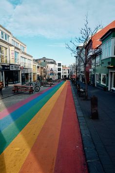 a rainbow painted street with benches and buildings in the backgroung, as seen from across the street