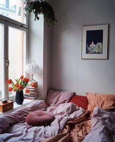 an unmade bed sitting in front of a window next to a potted plant