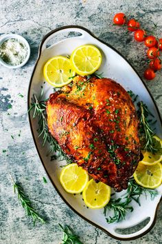 a chicken with lemons and herbs on a white plate next to some small bowls